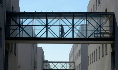 Uma mulher caminha numa ponte transparente, entre dois edifícios. Mais pontes iguais surgem em perspetiva no fundo da imagem.