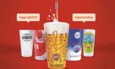 Um copo de cerveja dourada Super Bock sendo servido, com espuma no topo e design gráfico vibrante, destacado contra um fundo vermelho, cercado por outros copos temáticos de festivais de música patrocinados pela Super Bock.