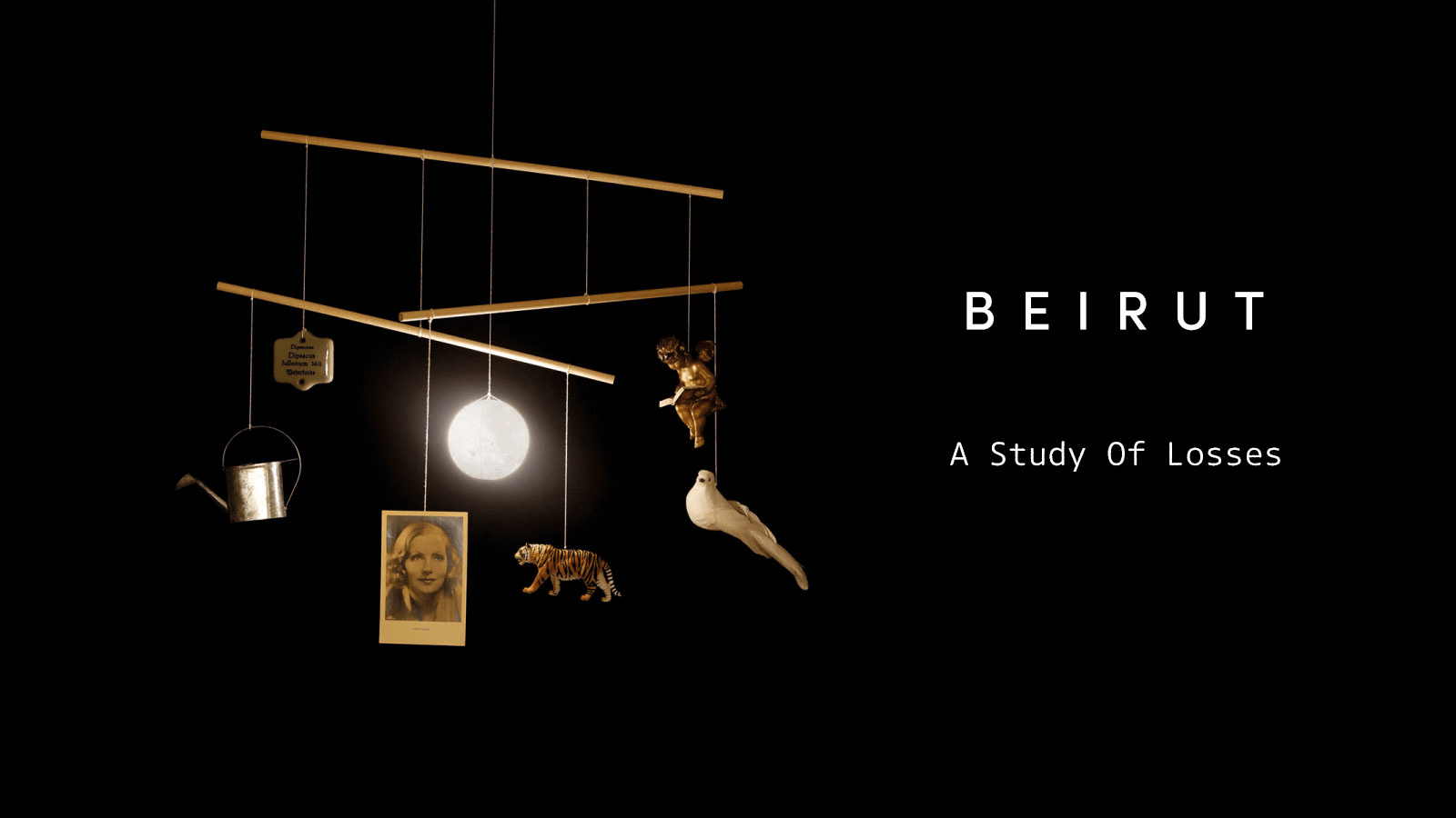 Capa do álbum A Study of Losses, da banda Beirut, mostrando um móbile suspenso sobre fundo preto. Os objetos pendurados — uma pequena lata de regador metálico, uma fotografia antiga de uma mulher, um tigre em miniatura, um anjo dourado, uma pomba branca e uma esfera luminosa — criam um equilíbrio delicado e simbólico. À direita, o nome “Beirut” e o título do álbum aparecem em tipografia branca minimalista.